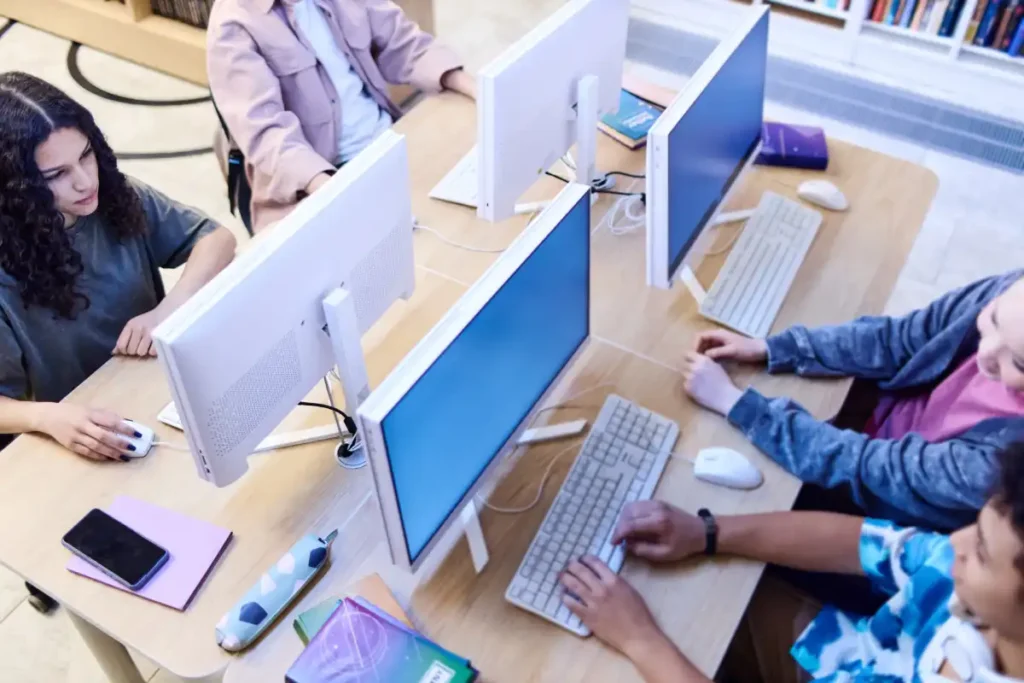 Students using desktop computers in a classroom to develop digital skills through guided instruction.