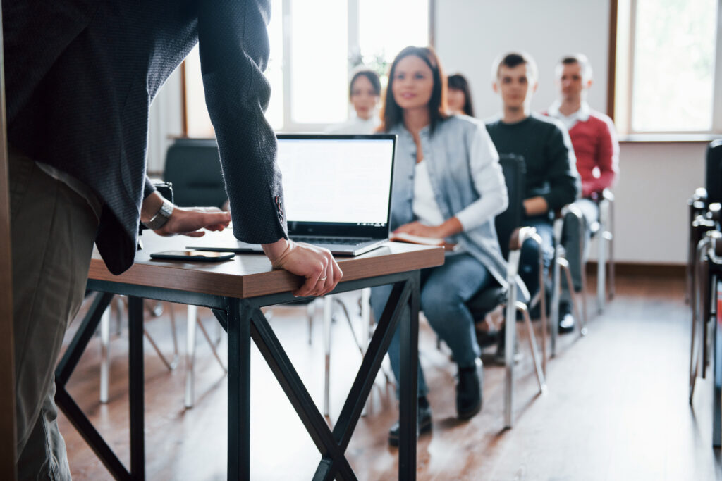 Instructor presenting from a laptop to an adult learning group seated in a classroom setting