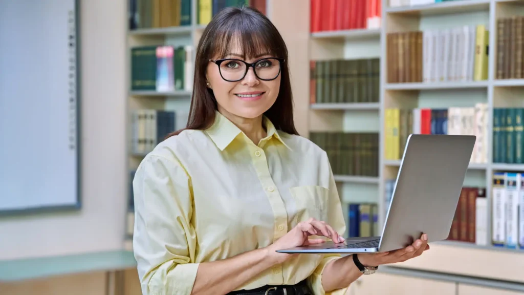 Professional educator holding a laptop in a library or academic learning environment