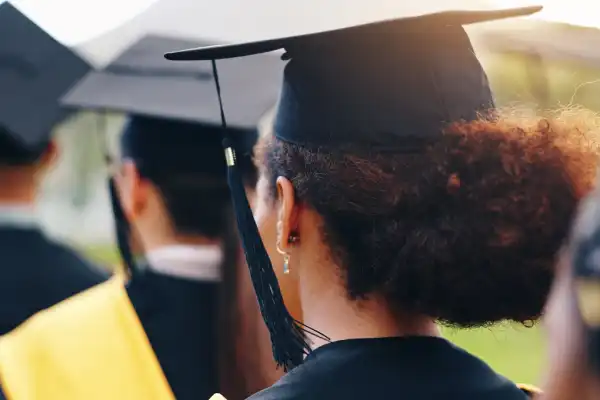 Graduate wearing a cap and gown at an outdoor ceremony, representing program completion and academic achievement.